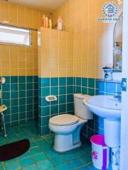 Compact bathroom with blue tile flooring and half-tiled walls featuring a toilet, sink, and small window