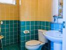 Compact bathroom with blue tile flooring and half-tiled walls featuring a toilet, sink, and small window