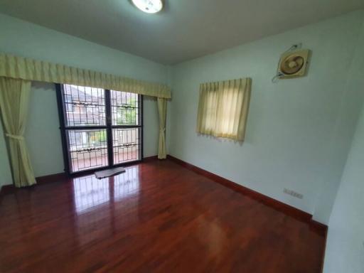 Empty bedroom with polished wooden floor, large windows, and white walls