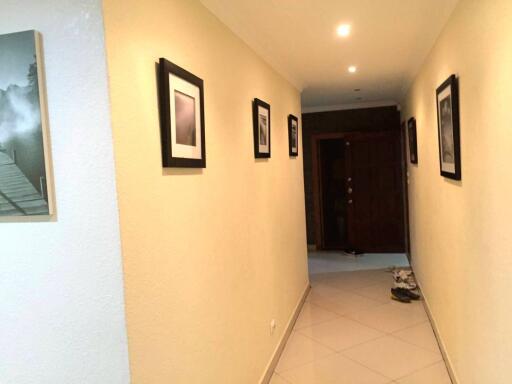 Bright and spacious hallway with tiled flooring and decorative wall frames leading to a wooden door