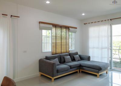 Spacious living room with modern grey sectional sofa and large window with wooden blinds