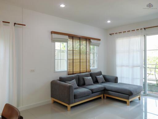 Spacious living room with modern grey sectional sofa and large window with wooden blinds