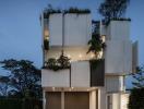 Modern multi-story residential building at dusk with beautifully illuminated balconies and a lush green rooftop garden