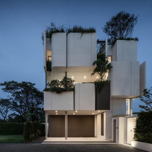 Modern multi-story residential building at dusk with beautifully illuminated balconies and a lush green rooftop garden