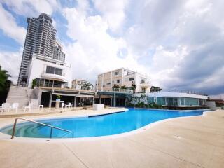 Swimming pool with surrounding lounge chairs and adjacent residential building under a cloudy sky