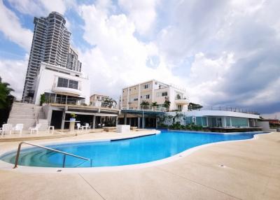Swimming pool with surrounding lounge chairs and adjacent residential building under a cloudy sky