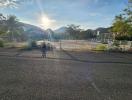 Sun setting over a paved area with fencing and mountain views