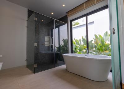 Modern bathroom interior with freestanding tub, walk-in shower, and greenery