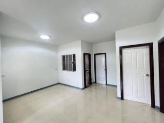 Spacious empty room with tiled flooring, bright ceiling lights, and multiple doors