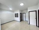 Spacious empty room with tiled flooring, bright ceiling lights, and multiple doors