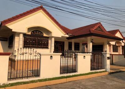 Elegant single-story residential house with red roofing and white walls behind a decorative iron gate