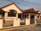 Elegant single-story residential house with red roofing and white walls behind a decorative iron gate