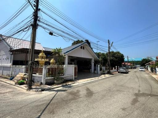 Suburban street view showing a house with white walls and a blue roof with carport