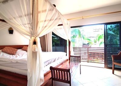 Spacious bedroom with large bed, white drapery, and balcony access featuring a view of lush greenery