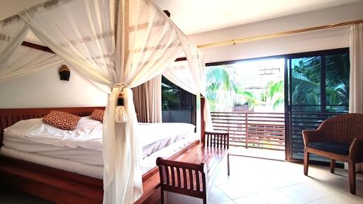 Spacious bedroom with large bed, white drapery, and balcony access featuring a view of lush greenery