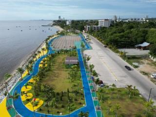 Aerial view of a vibrant coastal park and walkway adjacent to a beach with city skyline in the background