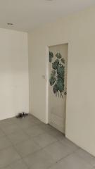 Spacious empty room with monotone walls and a door featuring a tropical leaf motif