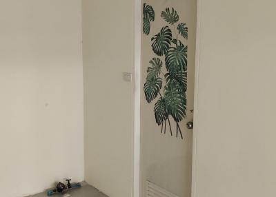Spacious empty room with monotone walls and a door featuring a tropical leaf motif