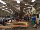 Spacious indoor market with rows of empty benches and various vendor stalls