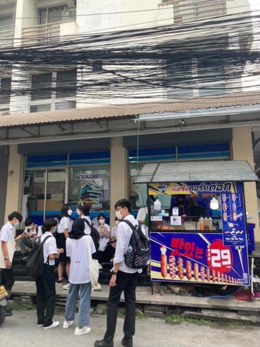 Busy street scene in front of a multi-story building with a food stand and people gathered