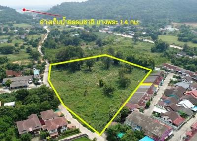Aerial view of a vacant land plot near a residential area with a lush green backdrop