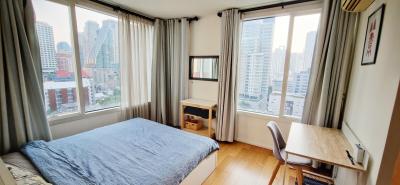 Modern bedroom with a city view, featuring a large bed, desk, and hardwood floors