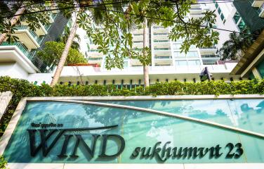 Exterior view of a modern residential apartment building with lush greenery and a clear sign reading 