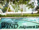 Exterior view of a modern residential apartment building with lush greenery and a clear sign reading 'WIND sukhumvit 23'