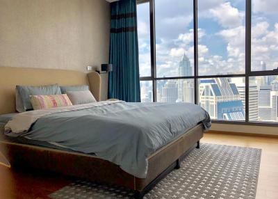 Modern bedroom with a large bed and floor-to-ceiling windows offering a city view