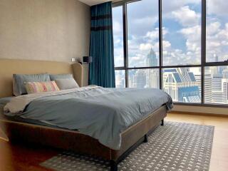 Modern bedroom with a large bed and floor-to-ceiling windows offering a city view