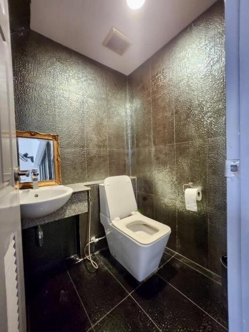 Modern bathroom interior with a shimmering tiled wall, toilet, and pedestal sink