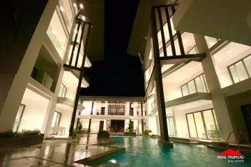 Modern residential building exterior at night with illuminated windows and a swimming pool