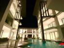 Modern residential building exterior at night with illuminated windows and a swimming pool