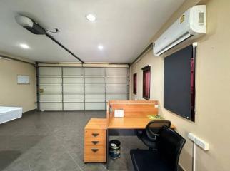 Compact bedroom with grey flooring, an office desk, air conditioning unit, and a roller shutter window