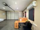 Compact bedroom with grey flooring, an office desk, air conditioning unit, and a roller shutter window