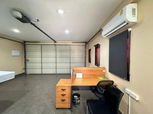 Compact bedroom with grey flooring, an office desk, air conditioning unit, and a roller shutter window