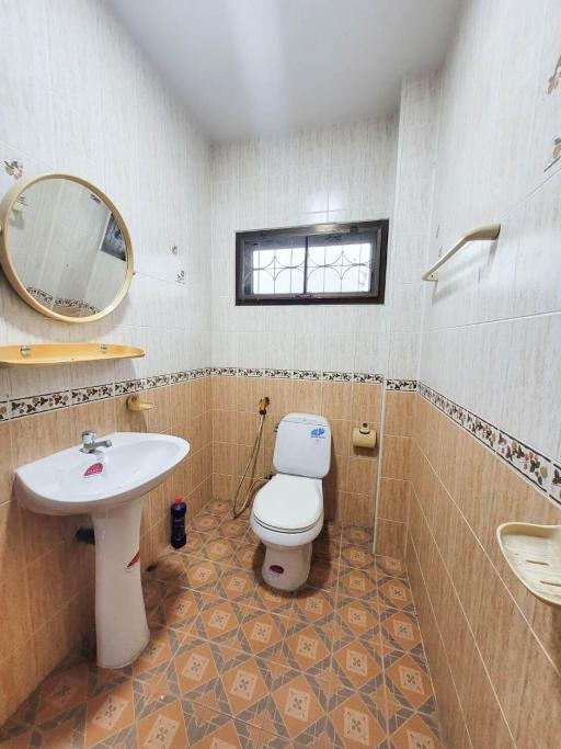 Compact bathroom with tiled flooring and walls, equipped with a sink, toilet, and mirror