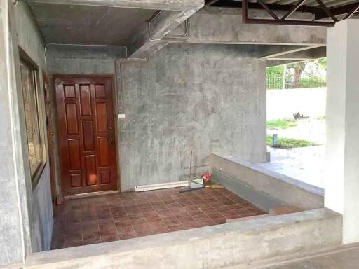 Concrete patio with brown tiled floor and a wooden entrance door