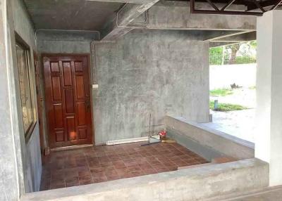 Concrete patio with brown tiled floor and a wooden entrance door
