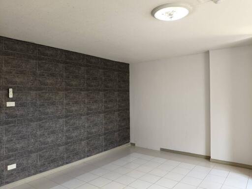 Spacious and empty room with tiled flooring and a dark-tiled accent wall