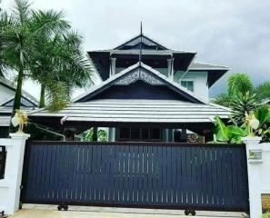 Traditional style house with a prominent gable roof behind a closed gate with palm trees