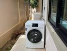 Outdoor laundry area with a modern washing machine beside a window