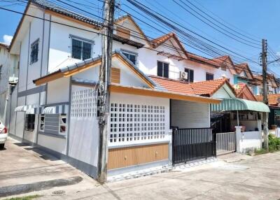 White two-story corner house with gated entrance and tile roofing under a clear blue sky