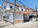 White two-story corner house with gated entrance and tile roofing under a clear blue sky