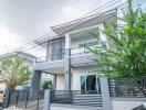 Modern two-story house with a sleek design and a gray color palette, featuring large windows and a secure fence