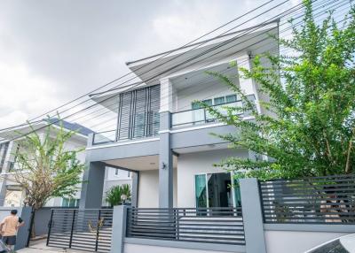 Modern two-story house with a sleek design and a gray color palette, featuring large windows and a secure fence