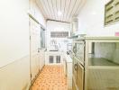 Narrow kitchen with white cabinetry and orange tiled flooring