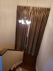 Elegant chandelier above staircase with wooden bannister and brown curtains