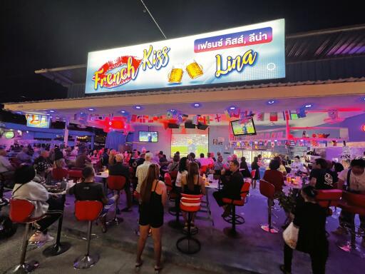 Busy outdoor restaurant at night with illuminated signage