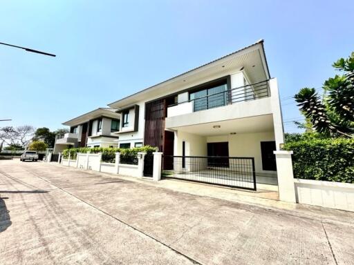 Modern two-story house with a white exterior, large windows, and a fenced-off lot